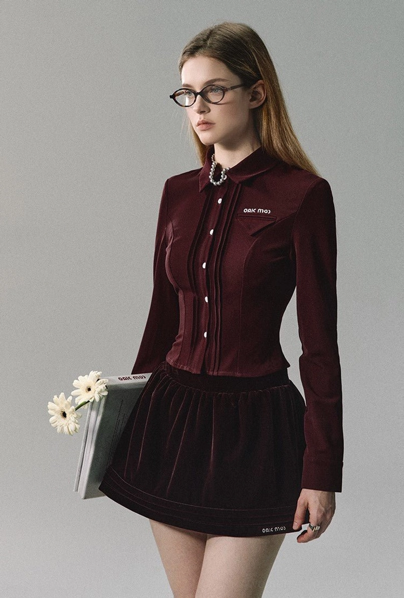 Burgundy velvet pleated mini skirt paired with a matching button-front long-sleeve blouse in an elevated streetwear outfit