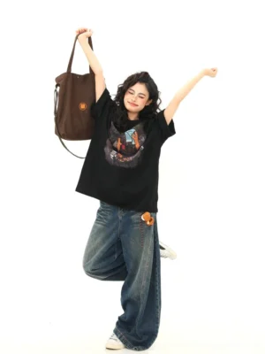 Oversized black campfire bear graphic T-shirt styled with wide-leg jeans and white sneakers in a playful streetwear outfit