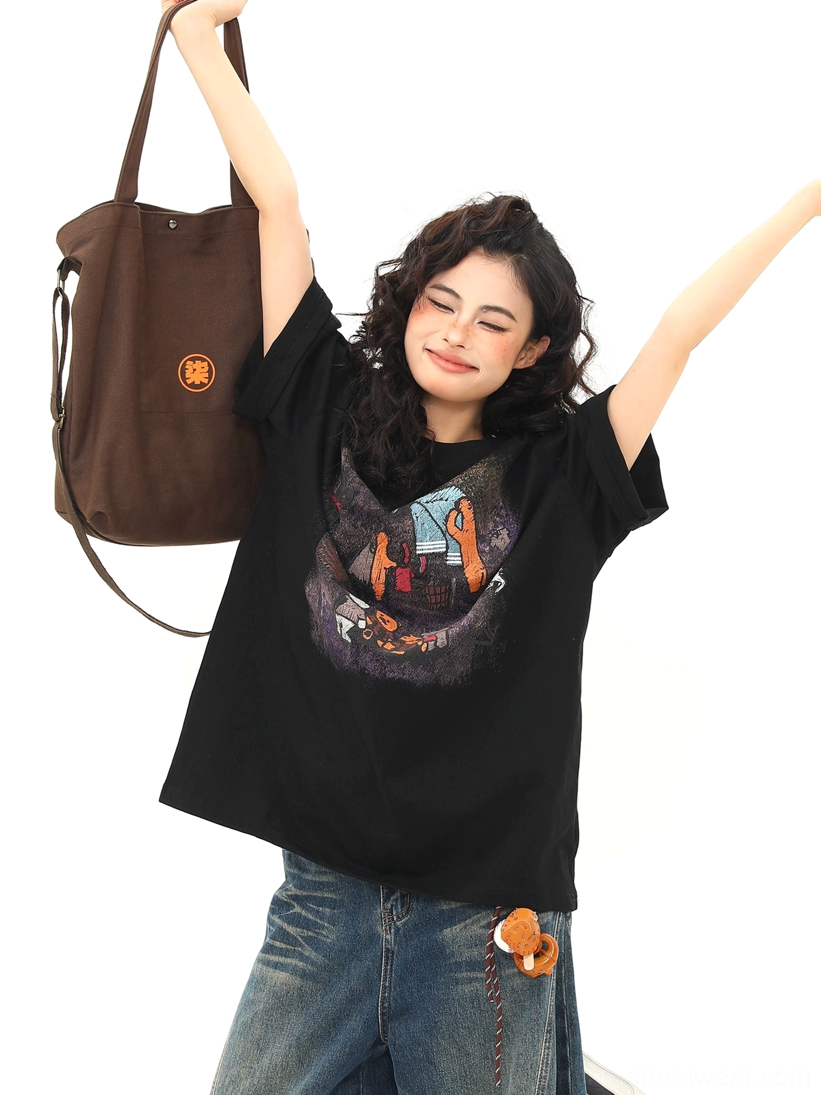 Black oversized streetwear T-shirt with playful campfire bear graphic and loose silhouette styled with wide-leg jeans