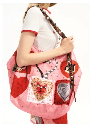 Candy pink kitty heart patchwork tote bag shown from the side with illustrated cat hearts, red heart graphics, silver heart details, and long beaded braided shoulder straps