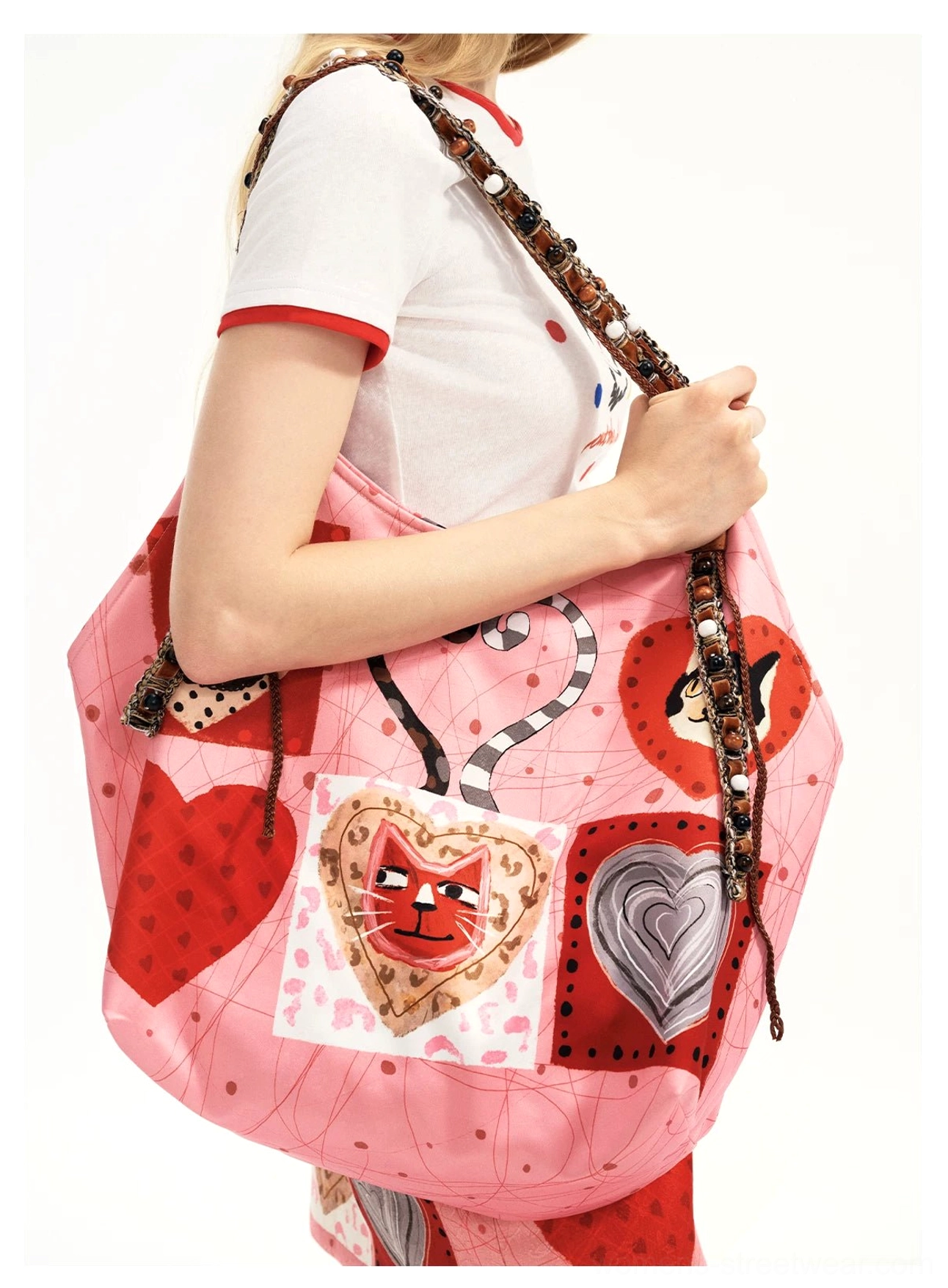 Candy pink kitty heart patchwork tote bag shown from the side with illustrated cat hearts, red heart graphics, silver heart details, and long beaded braided shoulder straps