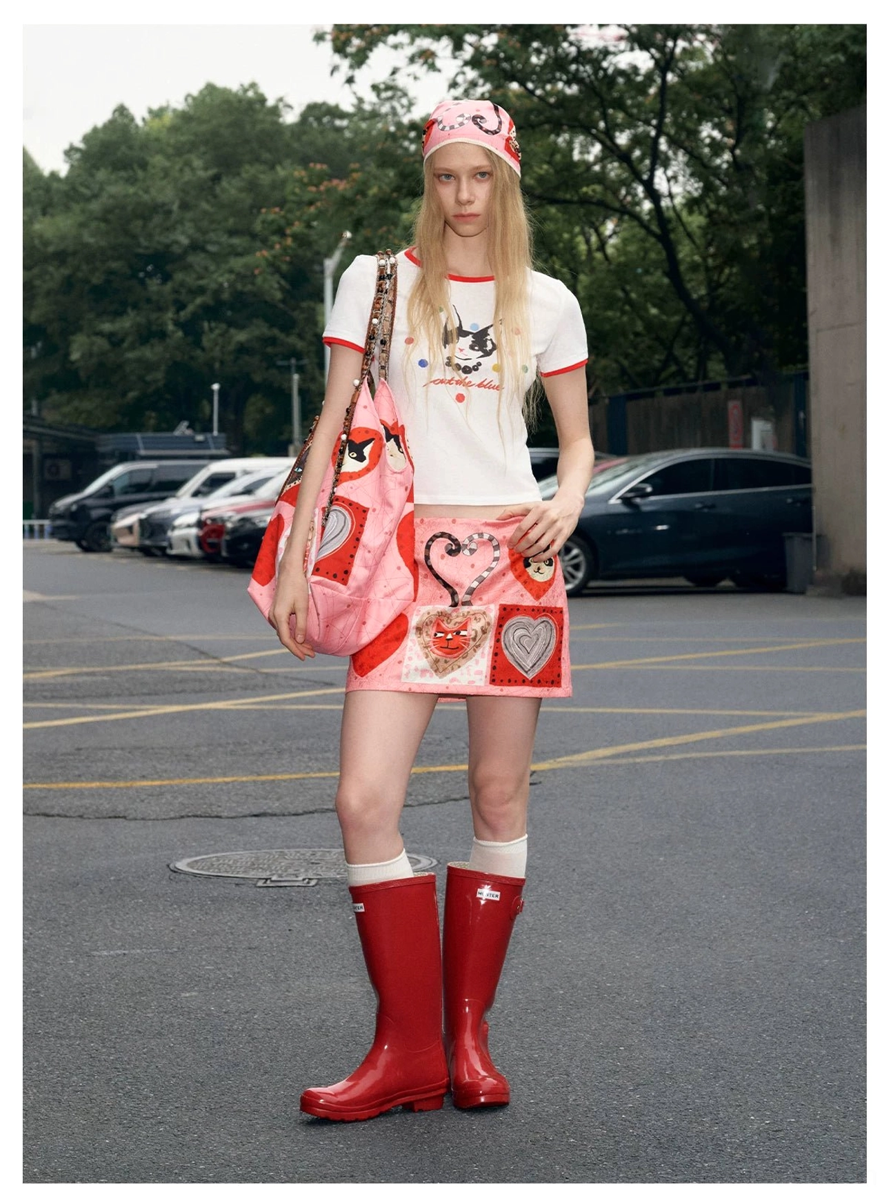 Full body Y2K streetwear outfit featuring a pink candy hearts kitty patchwork tote with ringer tee, heart print mini skirt, red rain boots, and matching headscarf