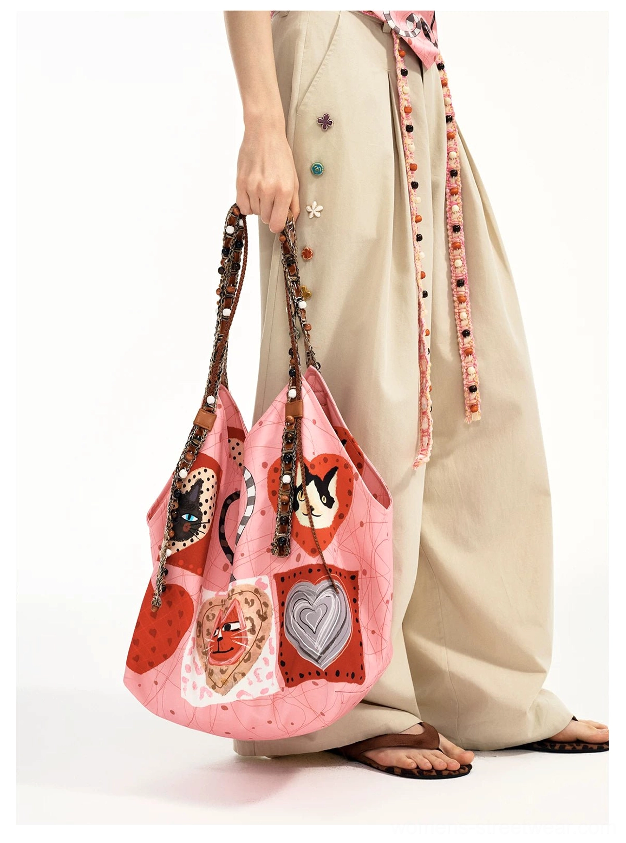 Close-up of the candy pink cat heart patchwork tote held by hand, showing the detailed beaded braided strap and matching decorative tassel styling
