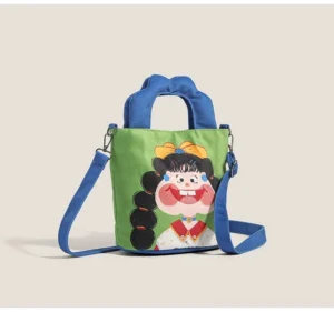 Cartoon girl canvas crossbody tote bag front three-quarter view with green body blue padded handles and playful black-lined girl print streetwear style