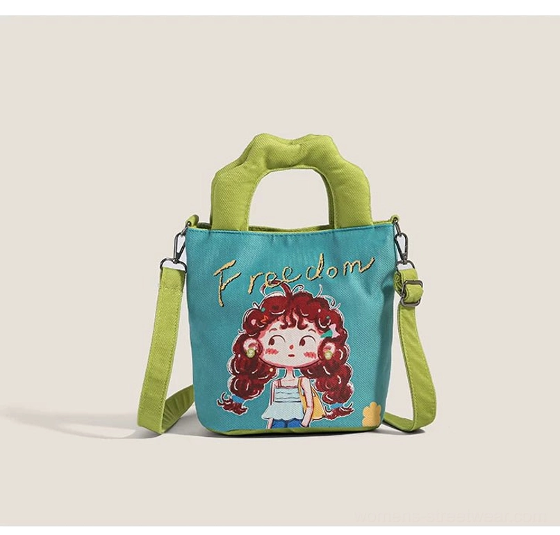 Teal blue cartoon canvas tote front three-quarter view with lime green padded handles and red curly-hair girl print featuring Freedom embroidery text