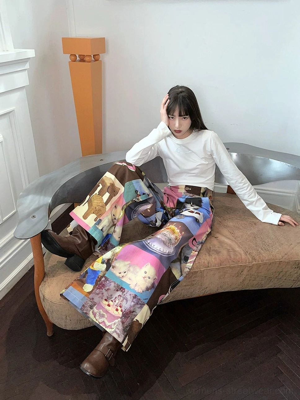 Seated side view showing the cat birthday cake graphic print on pink patchwork wide-leg streetwear pants