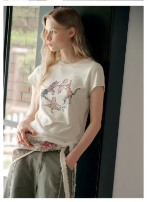 Light oatmeal cat graphic cropped tee styled with army green wide-leg jeans and a fringed floral waist scarf in a Korean streetwear outfit