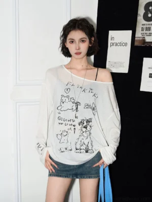 White cat graphic off-shoulder sheer long sleeve streetwear blouse worn with a denim mini skirt in a studio front view