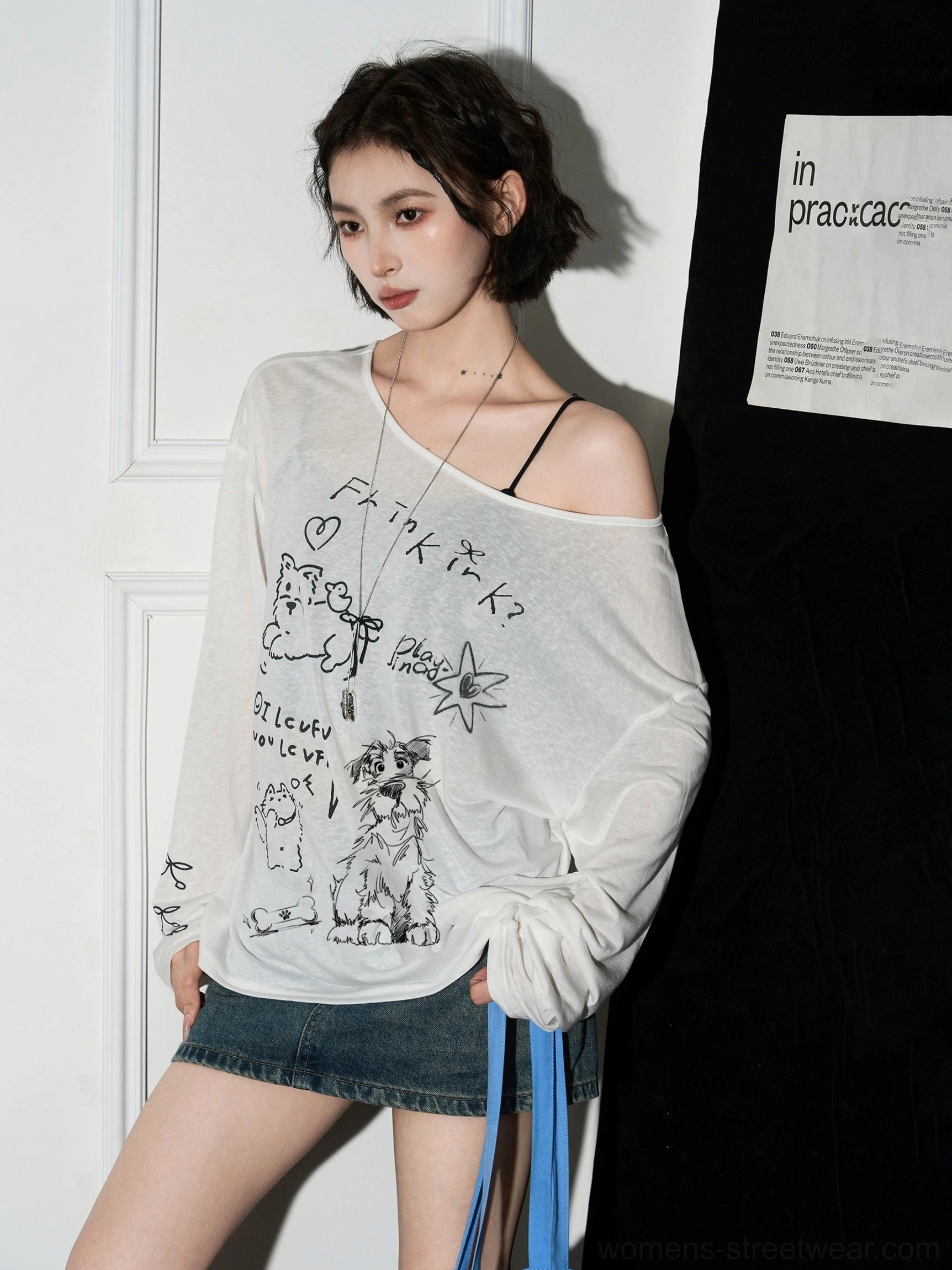 Side view of white semi-sheer cat graphic off-shoulder long sleeve blouse showing exposed shoulder and printed sleeve cuff