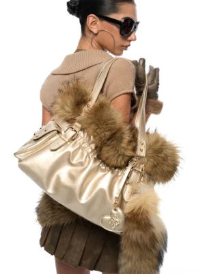 Champagne metallic faux fur tote bag with brown fluffy trim worn on model's shoulder, showing back view with ruched leather body and oversized fur tail charm