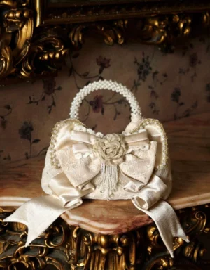 Champagne pearl handle rosette bow mini handbag displayed front view on a vintage carved wooden table