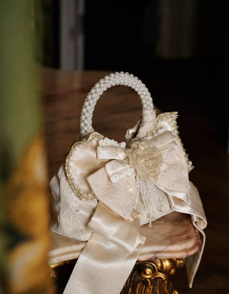 Side flat lay of champagne pearl handle rosette bow mini handbag showing lace texture and bead tassel