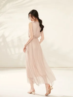 Rear three-quarter view of a champagne pink silk midi dress with elasticated high waist flowing asymmetric hem and nude block heel mules
