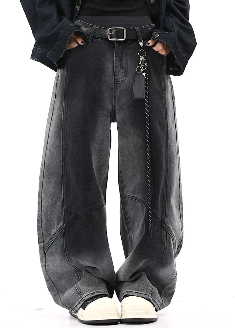 Front full-body view of charcoal black faded wide-leg denim streetwear pants with curved panel seams, black denim jacket, chain belt, and sneakers