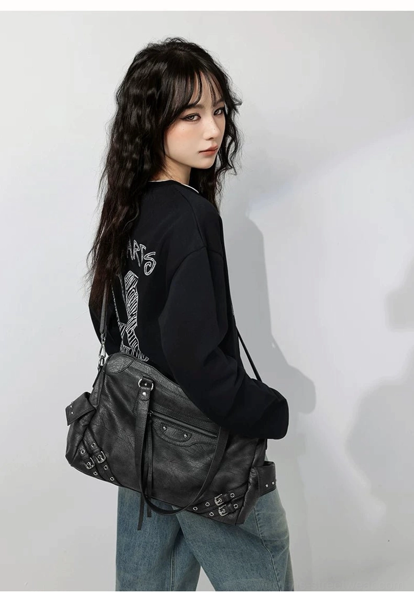 Charcoal buckle rider tote bag worn crossbody from the back with corner studs and relaxed daily streetwear styling