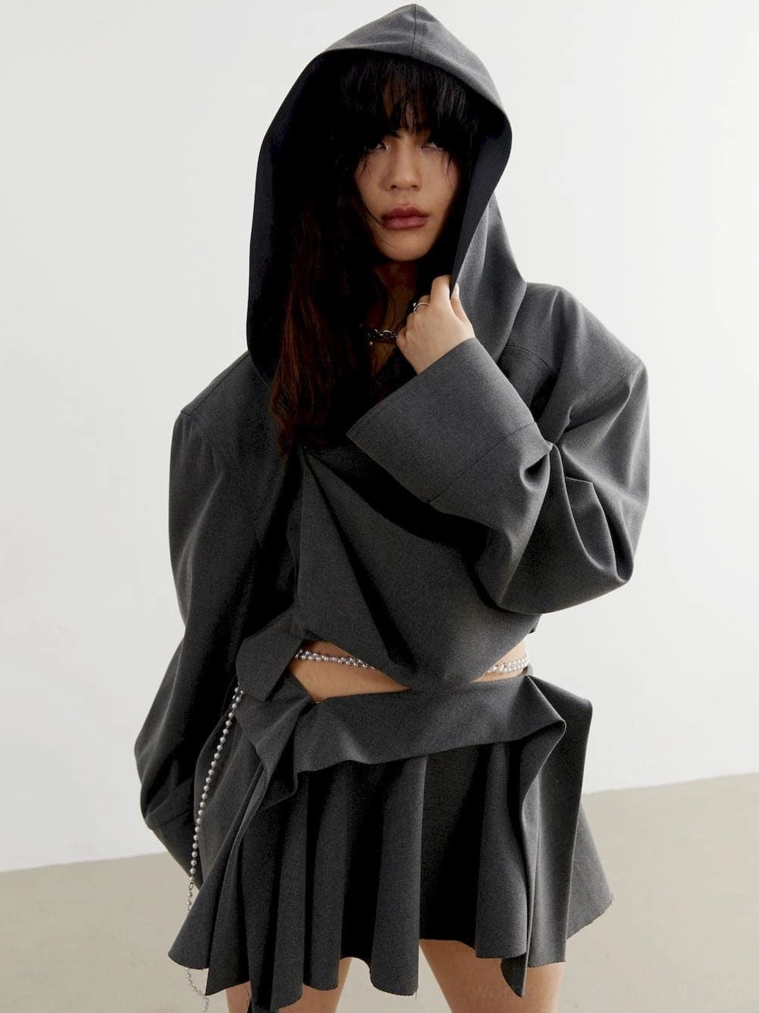 Charcoal cropped hoodie with structured pleated skirt styling, exposed midriff, pearl waist chain, and oversized hood
