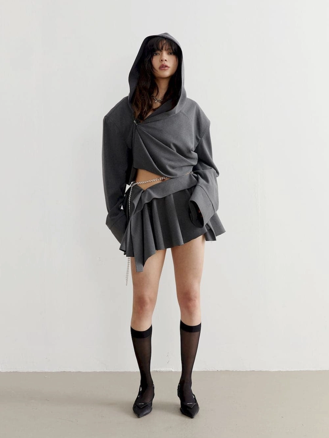 Full front view of charcoal cropped oversized hoodie styled with a pleated mini skirt and loose black socks for Y2K streetwear