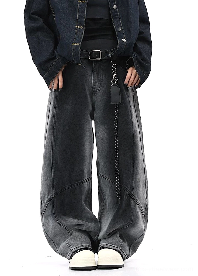 Full-body view of charcoal faded wide-leg streetwear pants with flowing draped legs, side seam details, black denim jacket, chain accessory, and sneakers