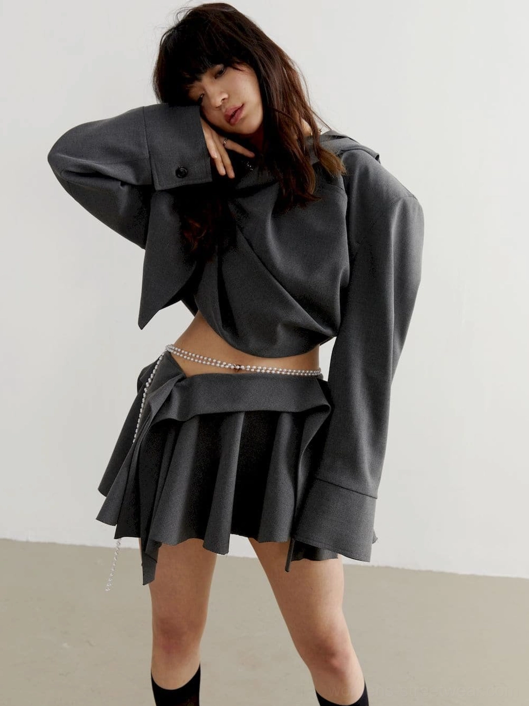 Three-quarter side view of charcoal gray cropped hoodie with relaxed oversized fit, draped hem, and pearl waist chain accent