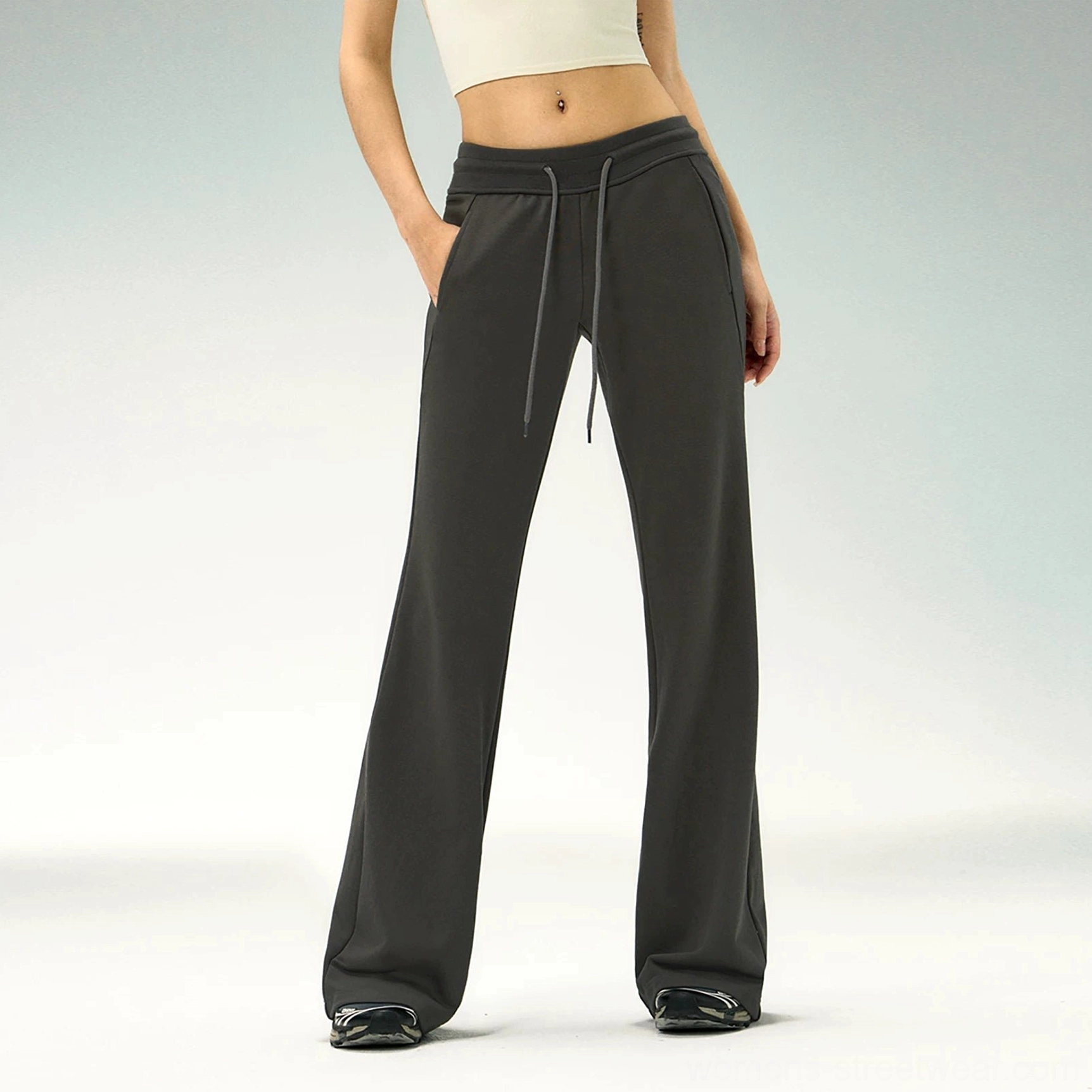 Front view of dark charcoal gray flared pants with side pockets, drawstring waist, tailored slim-to-flare fit, beige cropped tank, and sneakers