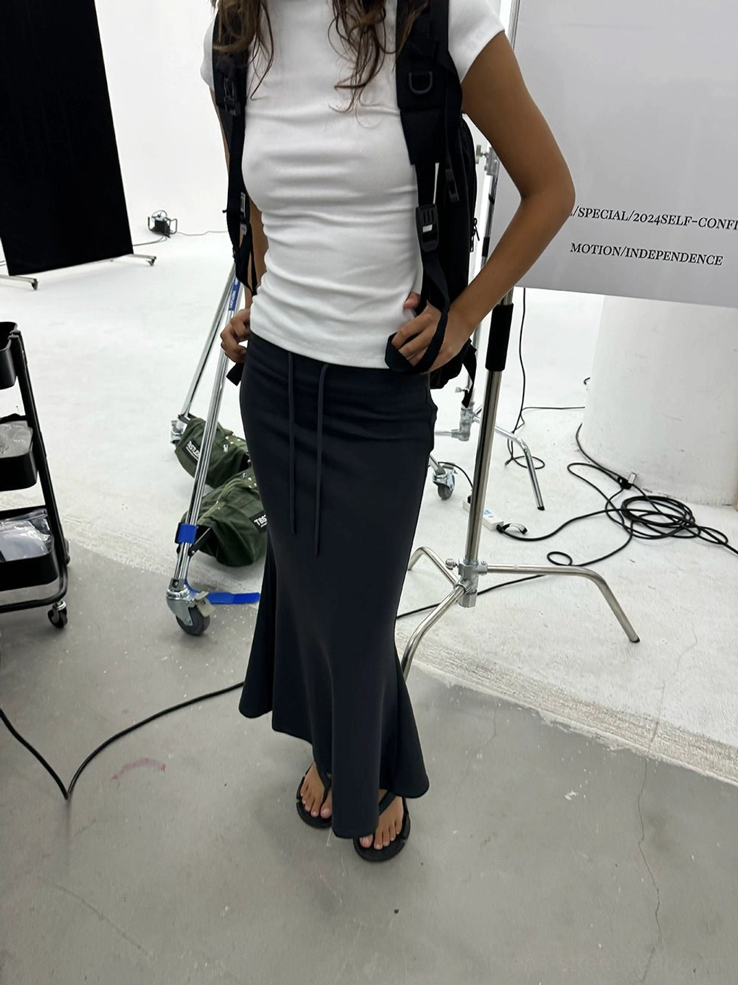 Dark charcoal gray slim fishtail maxi skirt shown in a front three-quarter detail view with a drawstring waistband and smooth stretch finish