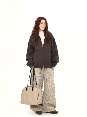 Relaxed female streetwear outfit featuring a half-zipped charcoal grey fleece hoodie, striped wide-leg pants, and beige tote bag