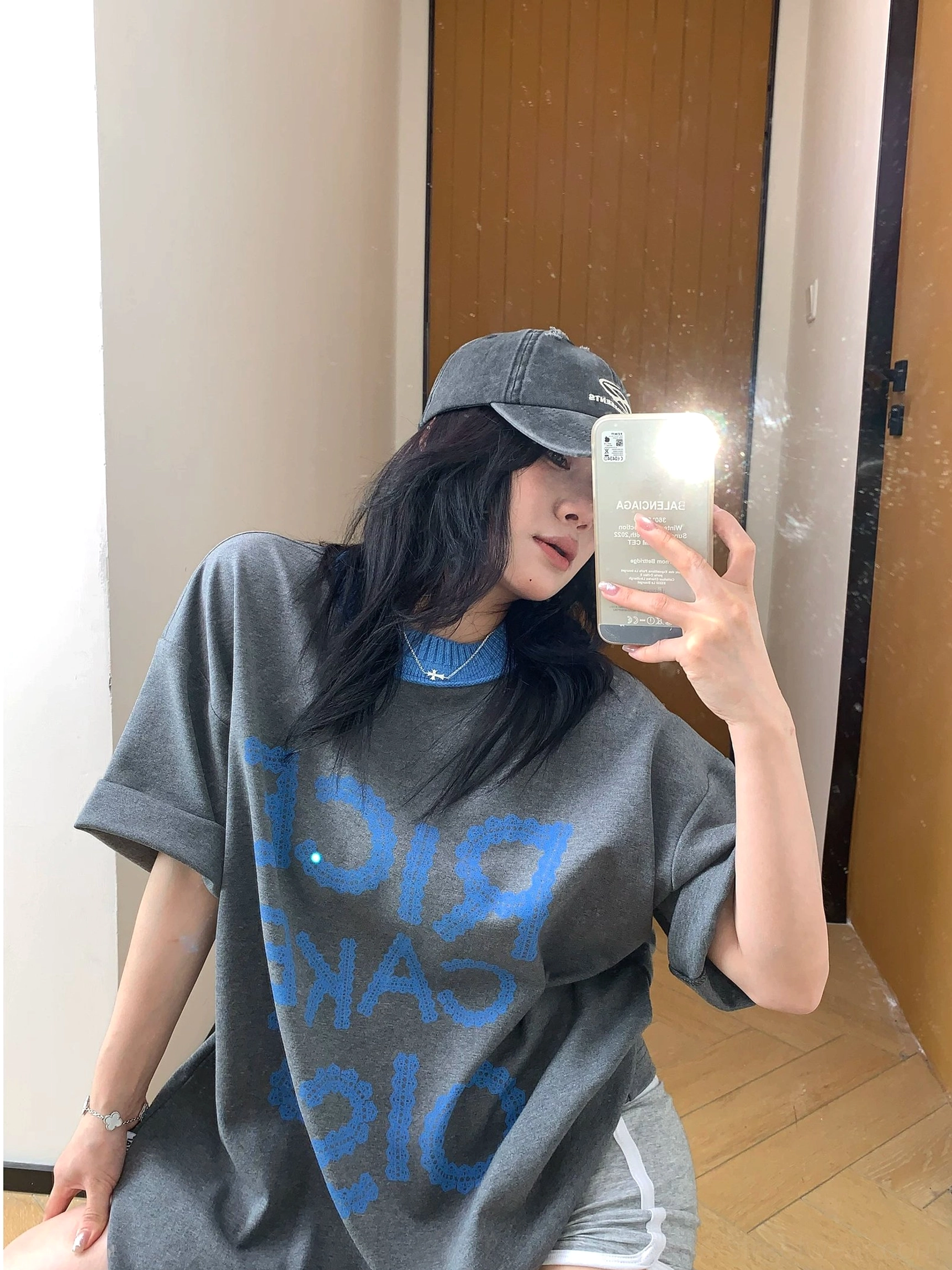 Charcoal oversized streetwear T-shirt with blue ribbed crew neck and rolled sleeves paired with light grey biker shorts and a vintage baseball cap