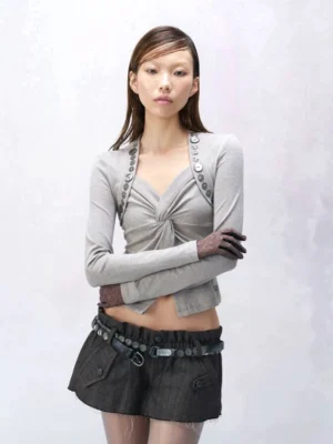 Model wearing a charcoal utility micro belt skirt with low-rise ruched waistband angled flap pockets raw frayed hem and gray twist-front knit top in a Seoul streetwear outfit