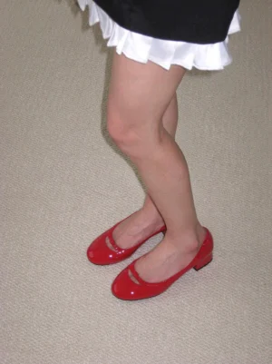 Women wearing cherry red glossy leather bow pumps with rounded toes and low block heels styled with a black ruffle mini skirt