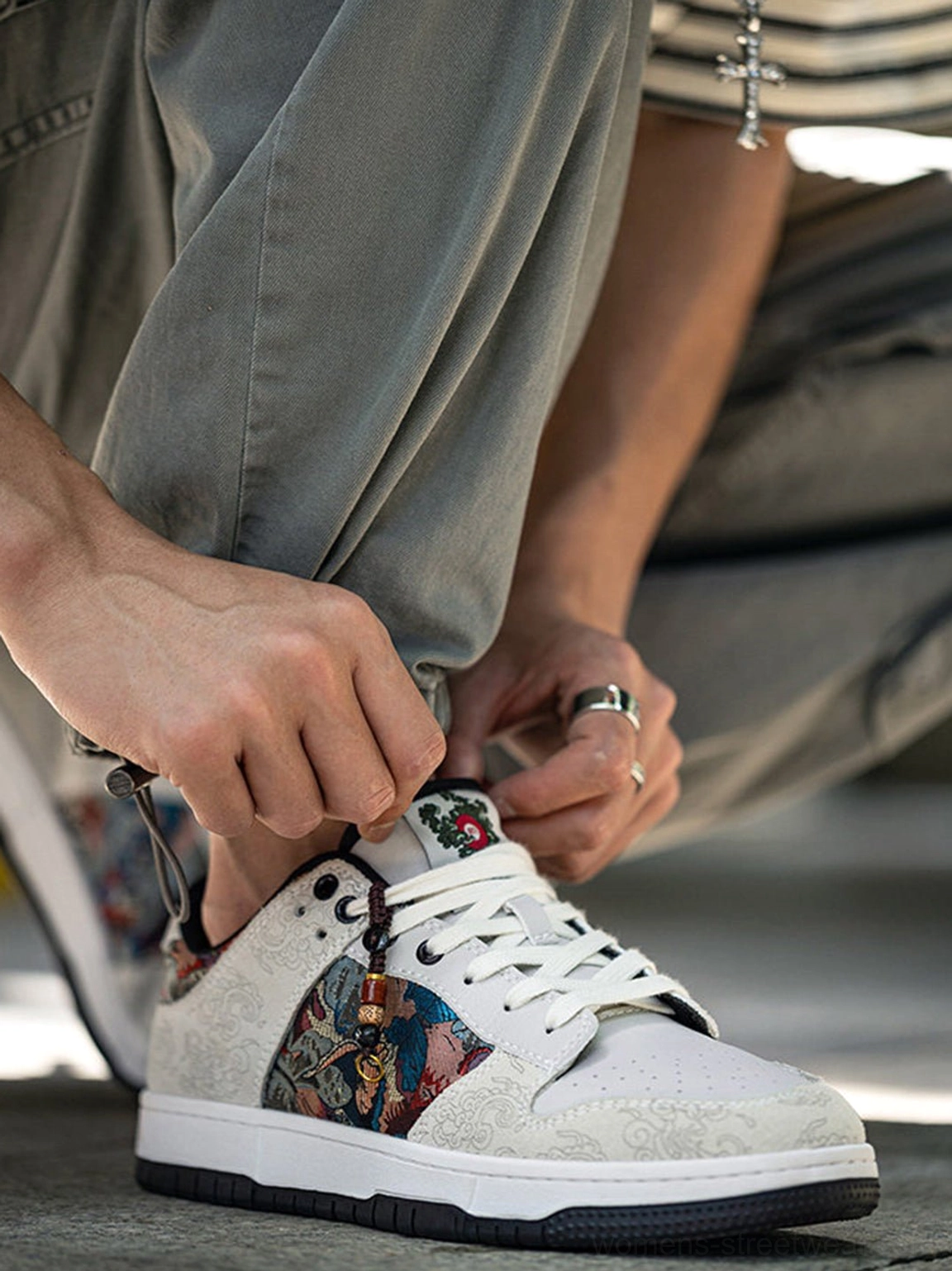 Close side view of Chinese embroidered bird brocade court sneakers with colorful textile embroidery while model ties shoelaces