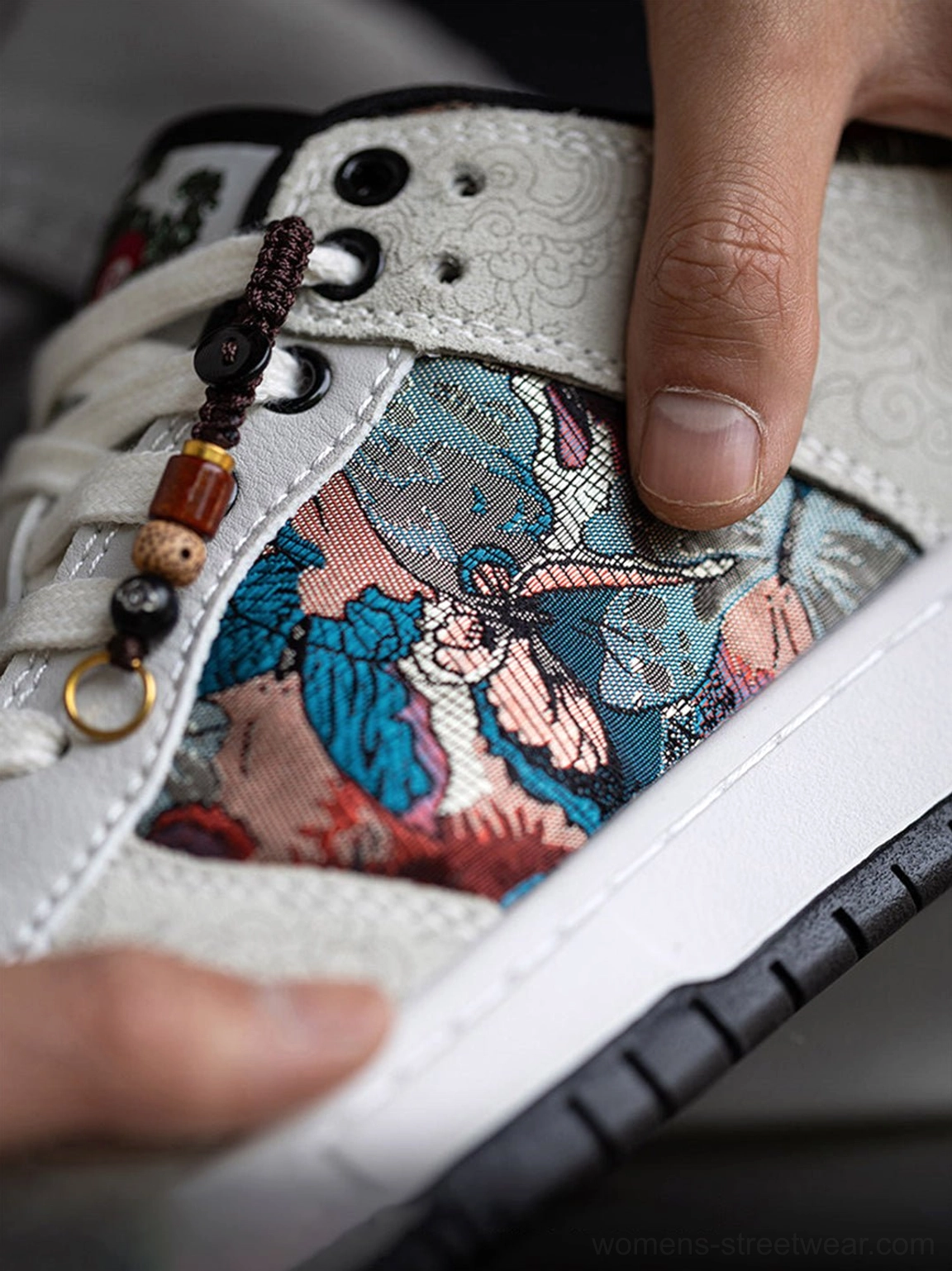 Extreme close-up of colorful bird brocade embroidery, eyelets, decorative lace charm, and white midsole on court sneakers