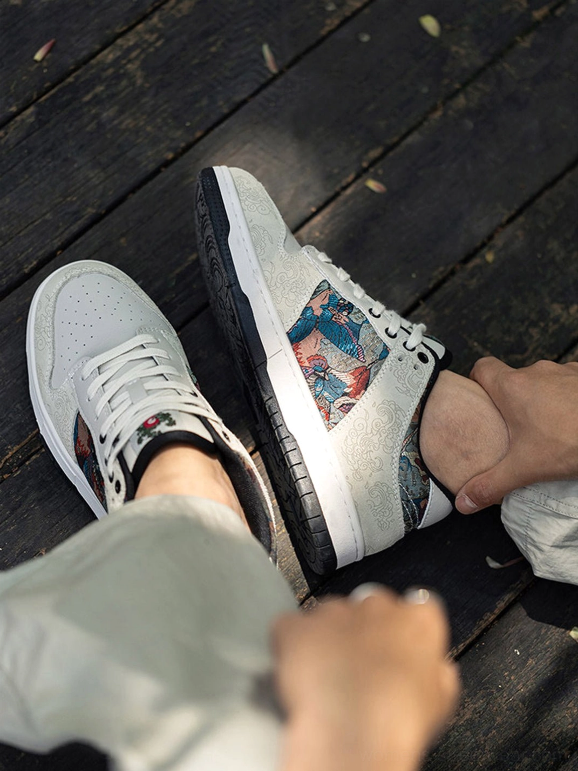Top view of white embroidered bird brocade streetwear court sneakers being worn with loose light grey pants and decorative lace detail