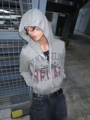 Choose Life distressed zip hoodie styled on an androgynous model in an industrial parking lot with the hood up and studded denim streetwear pants