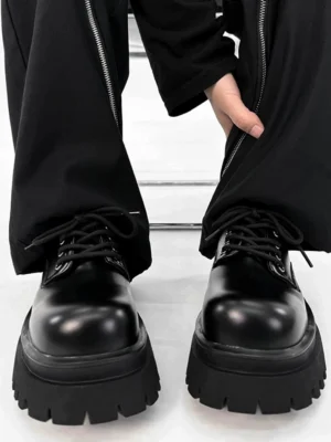 Chunky black platform derby shoes worn with black zippered wide-leg pants, showing polished synthetic leather uppers, rounded toes, lace-up fronts, and thick lug rubber soles