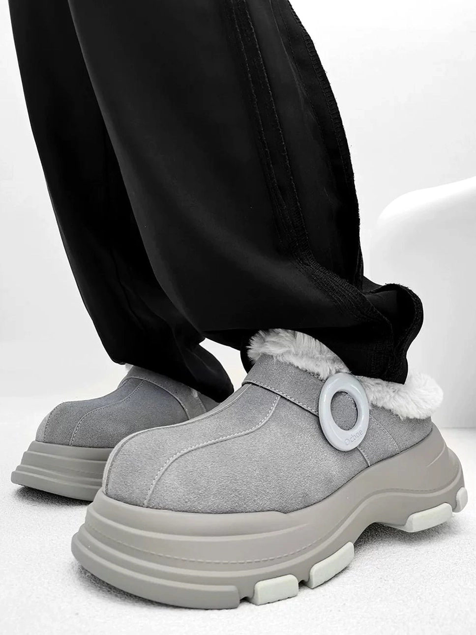 Two color options of chunky fleece-lined platform clogs styled with black casual pants, highlighting the elevated winter streetwear outsole