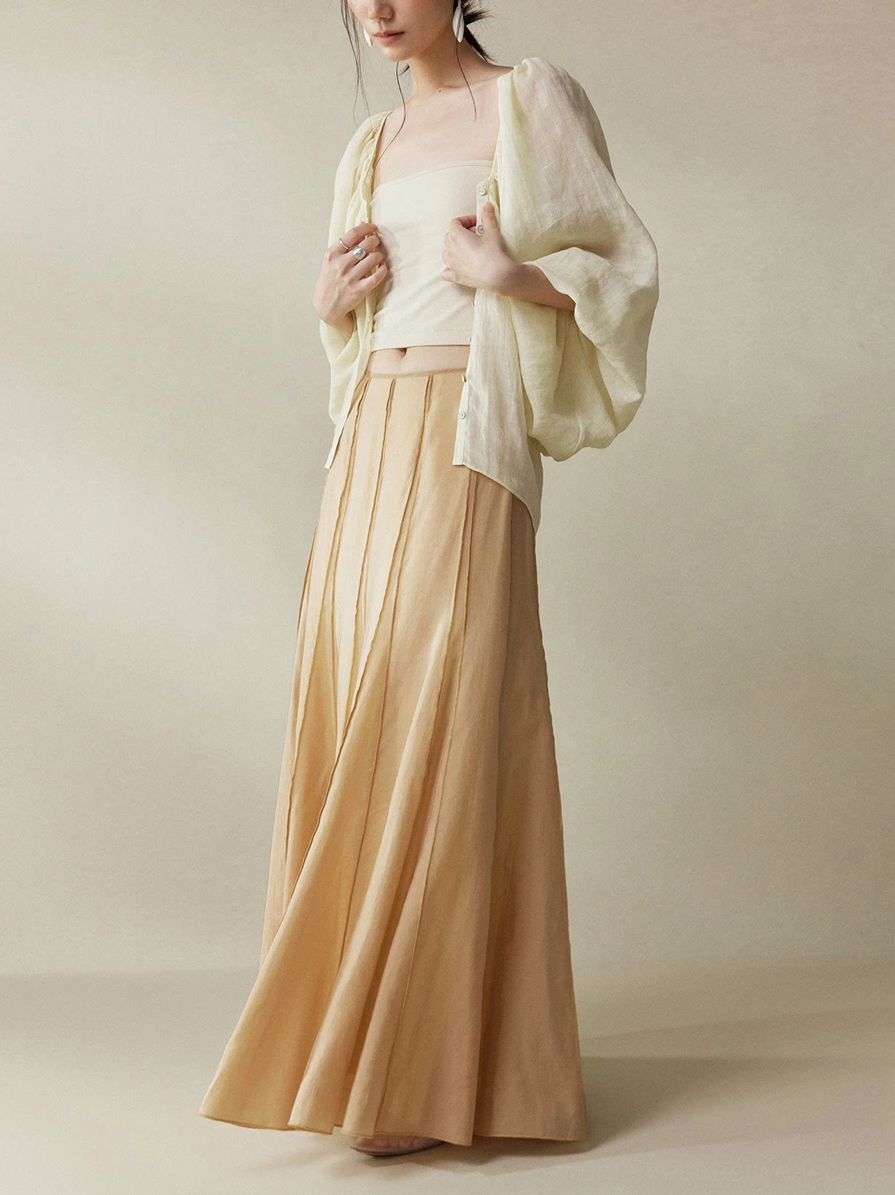 Cinnamon Brown cupro fishtail maxi skirt shown in a full body side profile styled with a cream camisole and light yellow cardigan