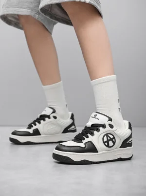 Model wearing black and white colorblock skate sneakers with perforated toe box and thick rubber sole on grey studio background
