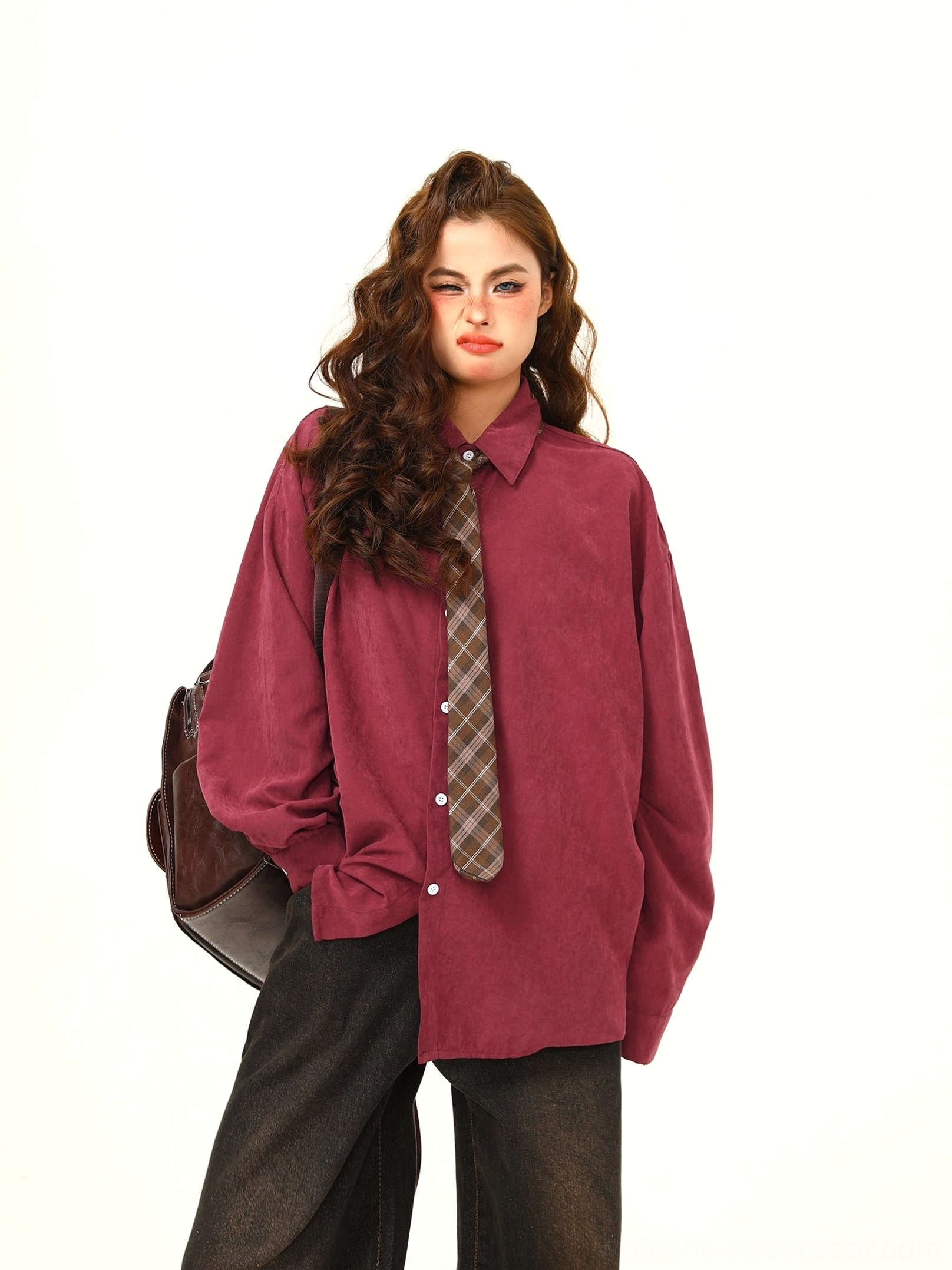 Front three-quarter view of claret oversized corduroy shirt with plaid brown necktie, loose long sleeves, white button placket, and shoulder bag