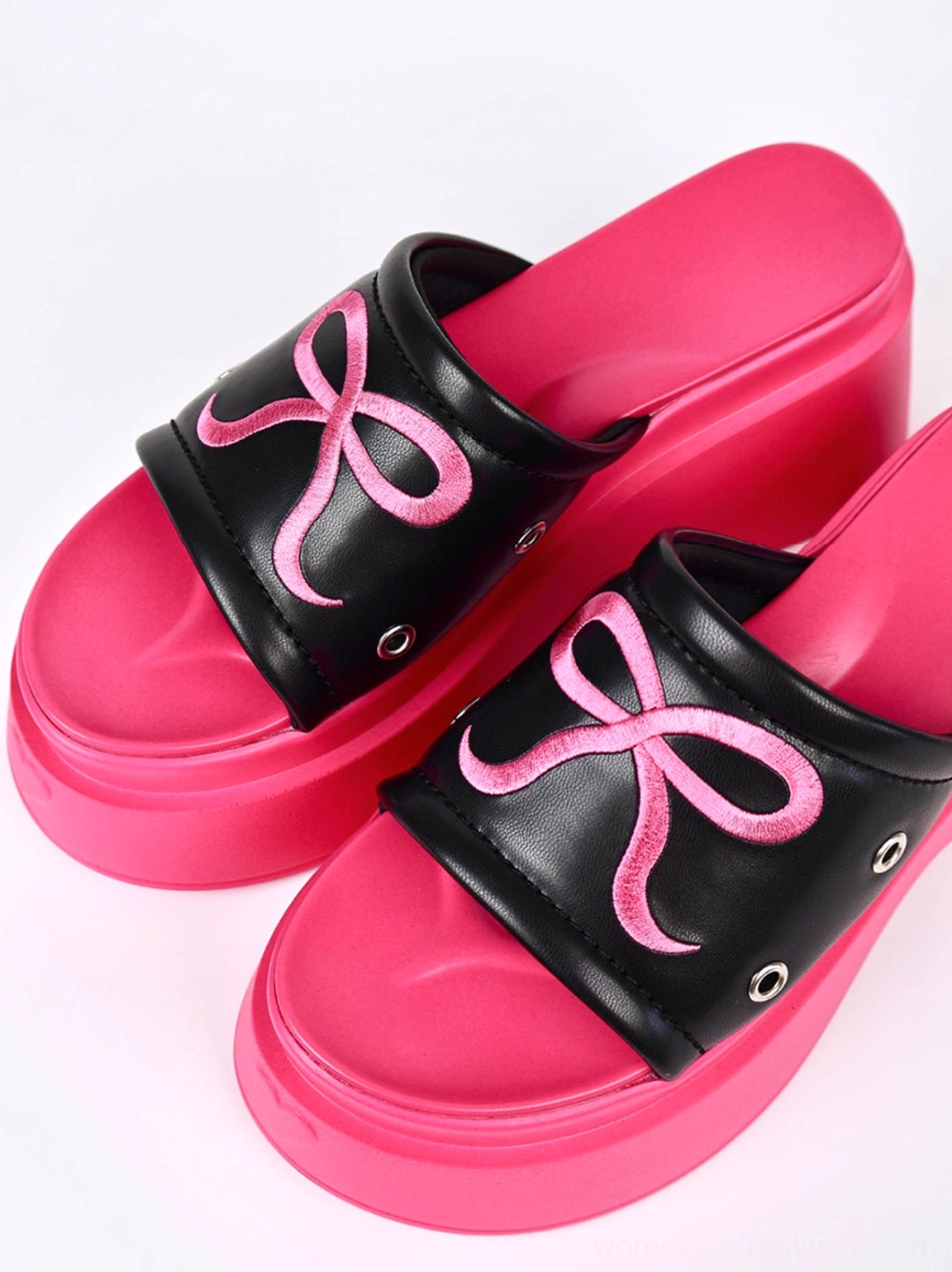 Close-up of hot pink bow embroidery, black strap, metal eyelets, and thick platform sole on Y2K slide sandals