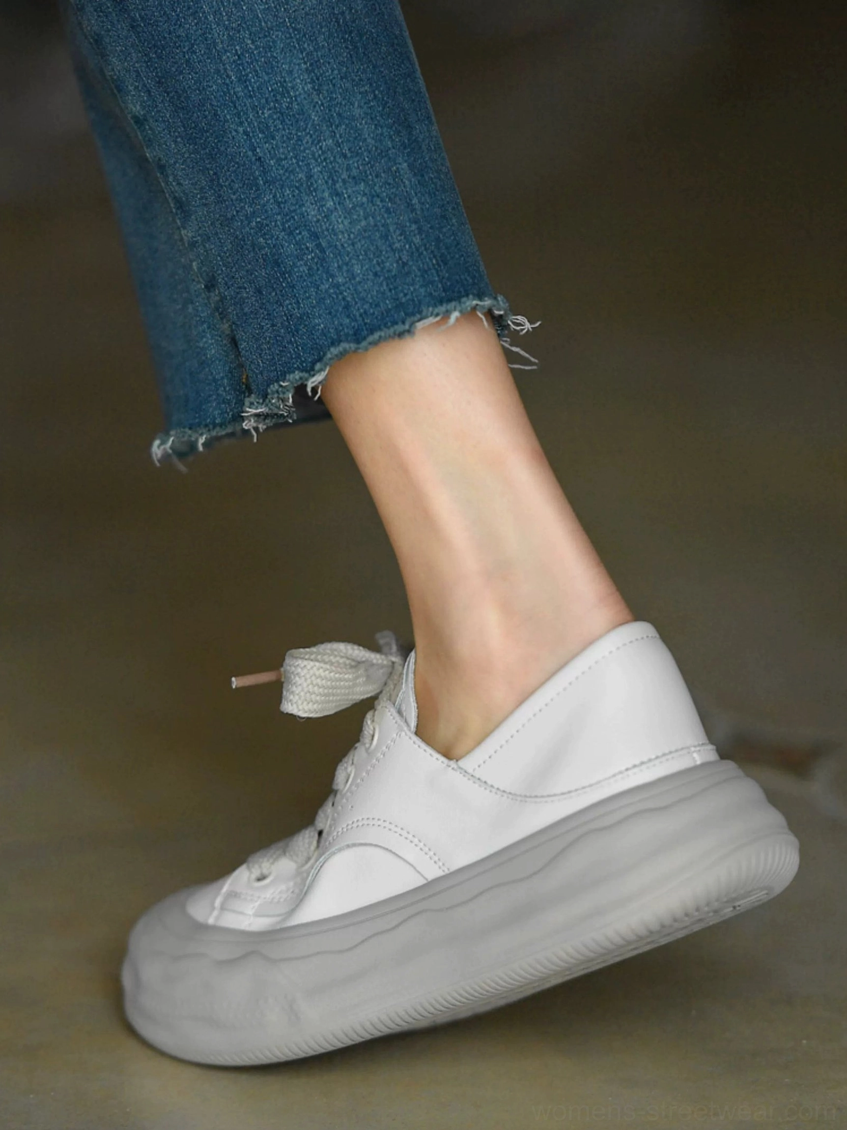 Low side view of grayish white chunky sneakers showing the foldable heel design, thick soft gray platform outsole, and cropped denim styling