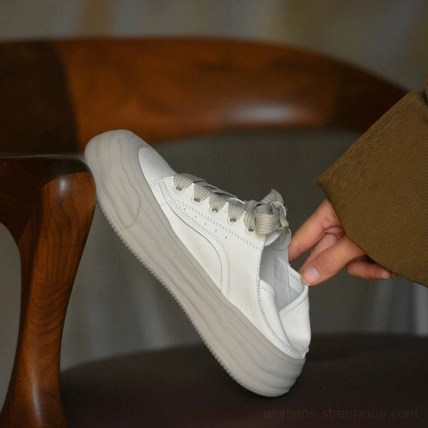 Handheld close-up of grayish white leather chunky platform sneakers with adjustable laces, distressed-look gray wave sole, and foldable heel