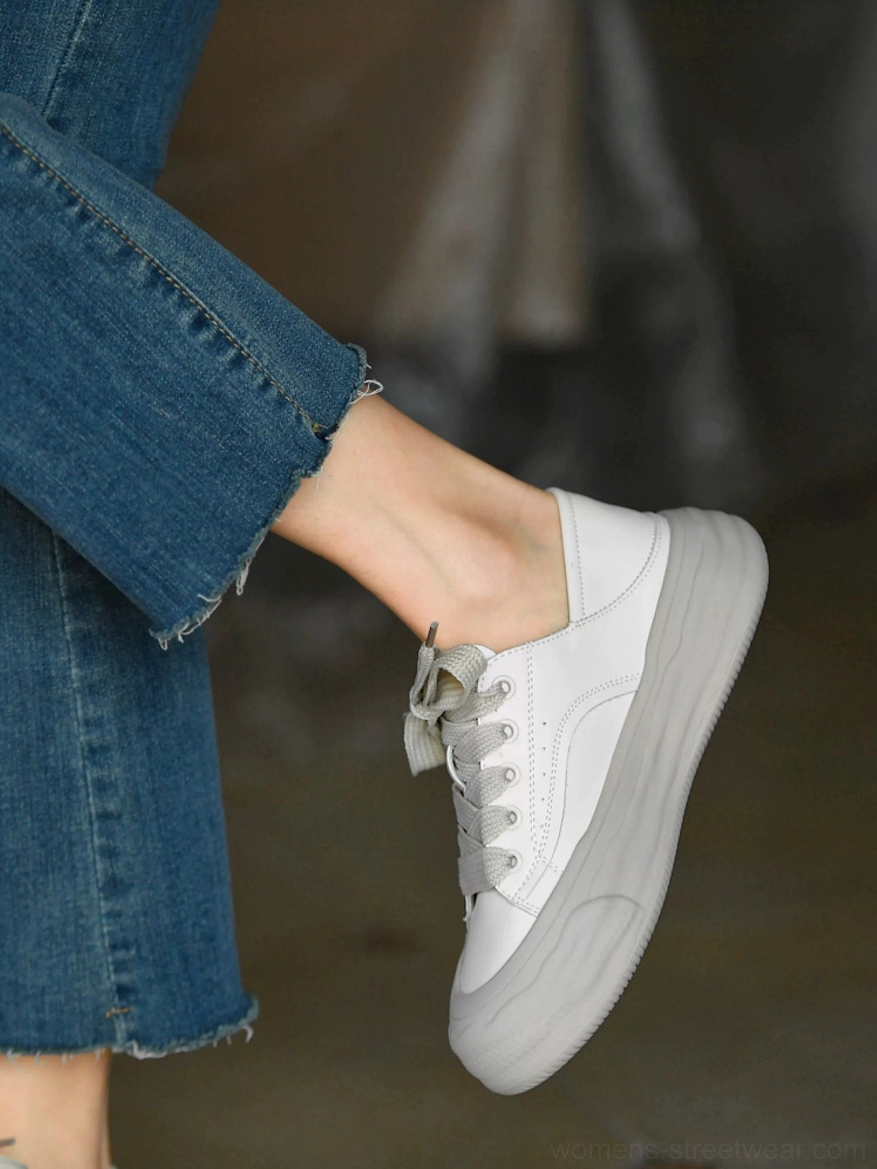 Grayish white platform sneaker on foot with frayed denim pants, featuring a round toe, gray laces, and thick sculpted streetwear sole