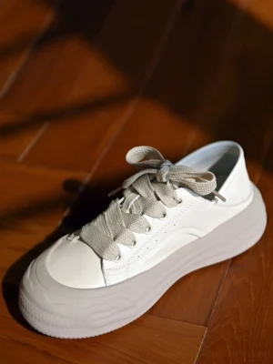 Top view of grayish white chunky platform sneakers with gray laces, foldable heel counters, smooth leather uppers, and sculpted wave rubber soles