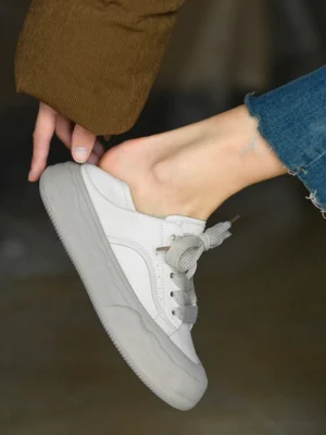 Side close-up of grayish white chunky platform sneakers worn with cropped denim jeans, showing the smooth leather upper and gradient gray rubber sole