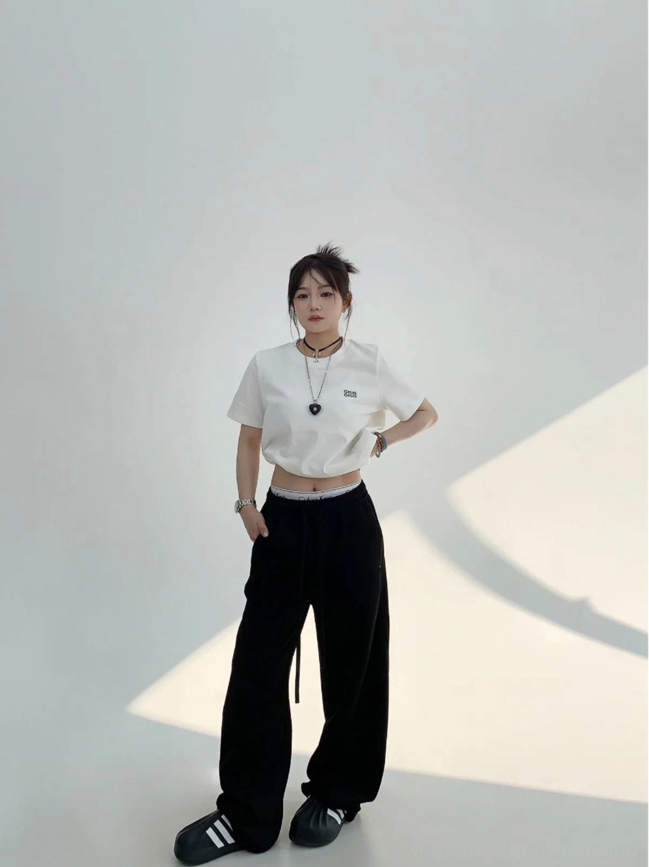 Black high-waist wide-leg cotton fleece streetwear sweatpants styled with a cropped white tee in a full-body front view