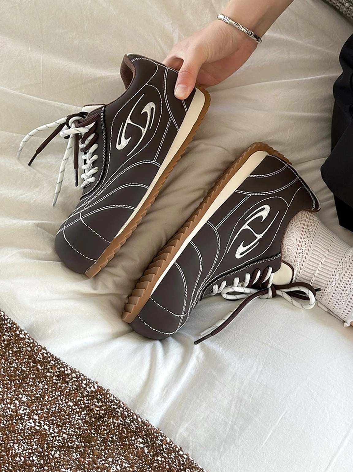 Close-up pair of coffee and beige double-lace low-profile retro trainers showing contrast stitching and gum soles