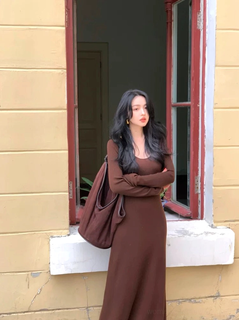Coffee brown fitted knit maxi dress with long sleeves and scoop neckline styled with a large brown tote bag by a vintage window