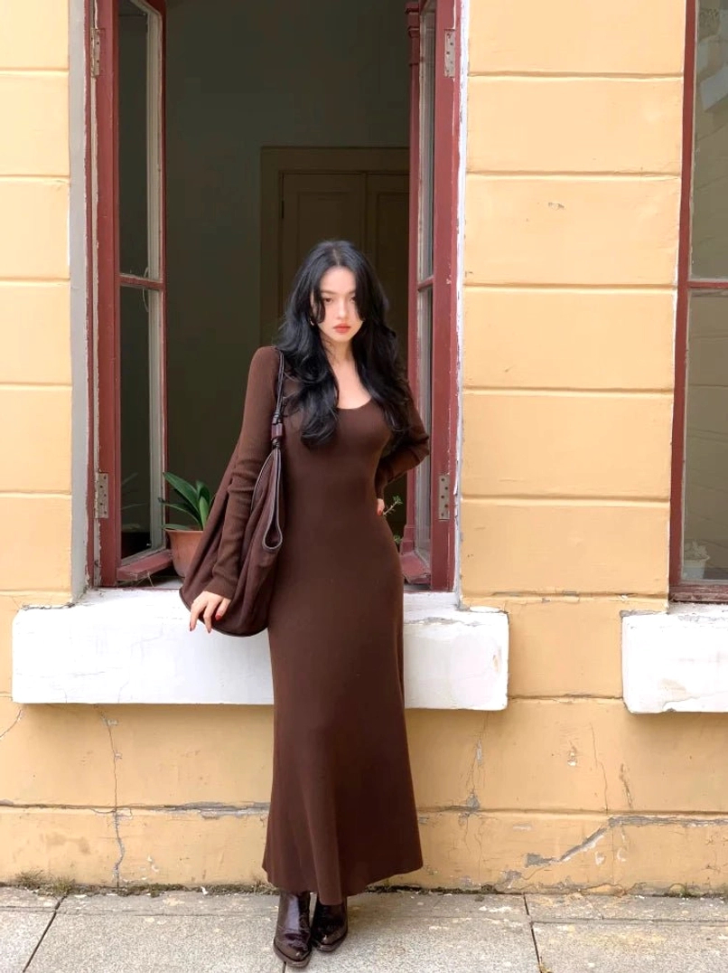 Coffee brown long sleeve scoop neck knit maxi dress shown in a full three-quarter front view outside a vintage building