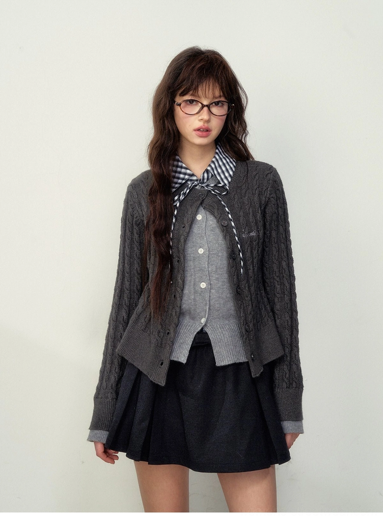 Close-up front view of college gray cable knit preppy cardigan with button closure and plaid bow styling