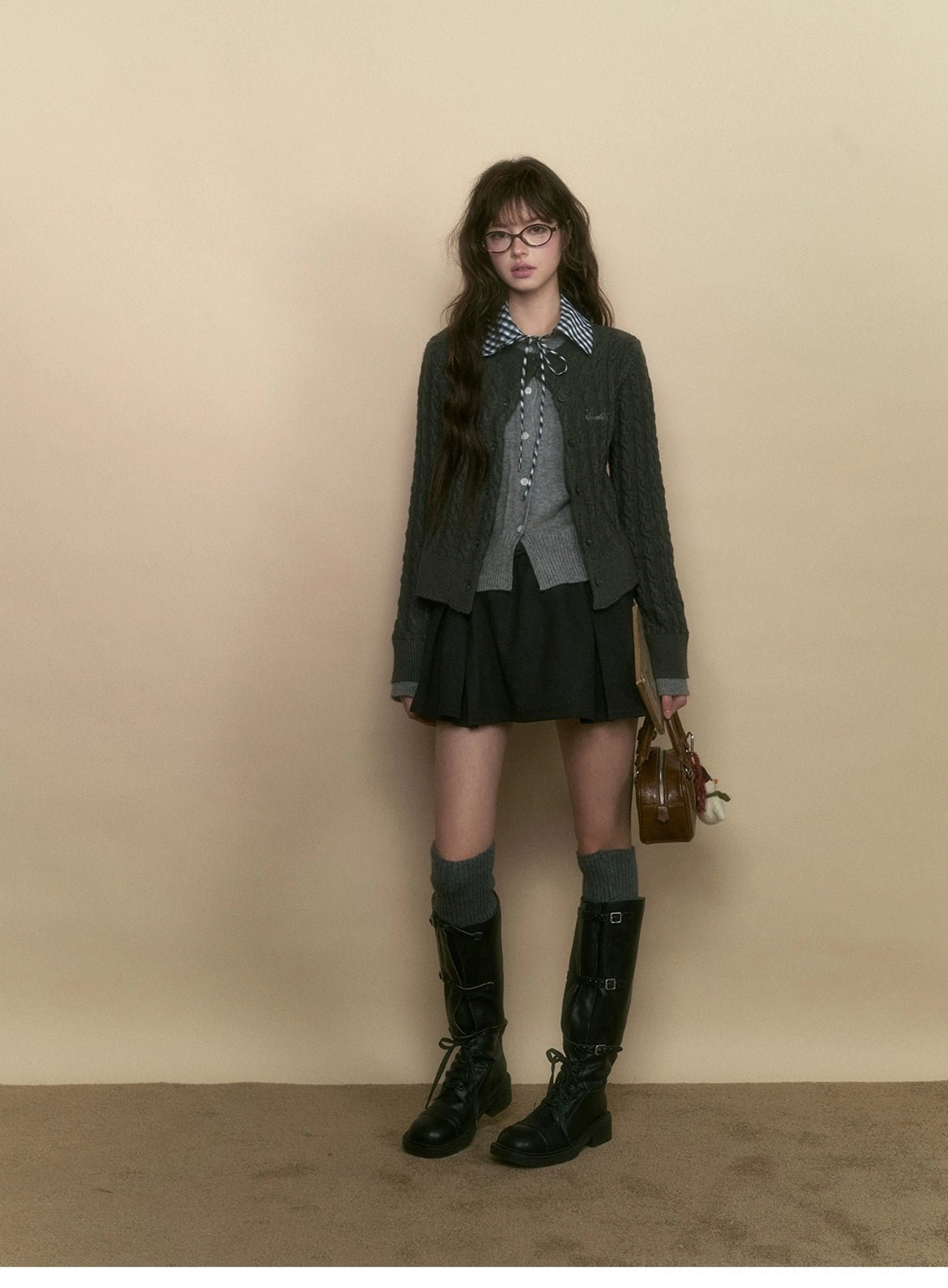 College gray cable knit preppy cardigan styled with a black pleated skirt and knee-high boots for dark academia